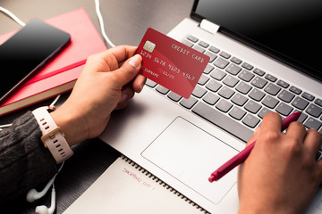Hands holding a red credit card and using the laptop for make payments online with security. Online...