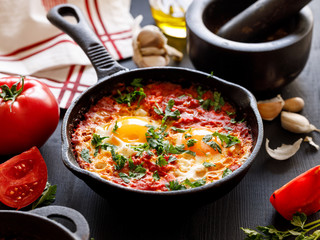 Shakshuka - traditional Middle Eastern dish based on tomatoes and eggs in a cast iron skillet close up view.