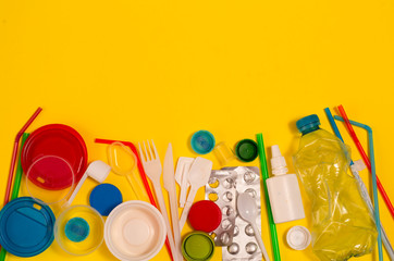White single-use plastic and other plastic items on a yellow background. The concept of choice...