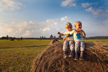 Naklejka na ściany i meble Happy twins on a haystack in a village at sunset. Happy kids in the field