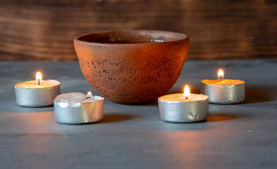 A ceramic bowl with tea and burning candles on a gray tabletop.