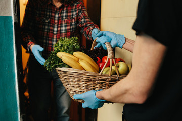 Online shopping concept. Male courier in black uniform and gloves with a grocery basket with fresh fruits, vegetables and greens. Home delivery food during quarantine coronavirus.