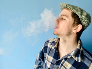 a young  man in checked shirt and retro hat smoking electronic cigarette