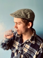 a young  man in checked shirt and retro hat smoking electronic cigarette