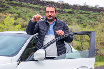 successful young happy man showing the keys standing near the car