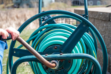 Selective focus on front bar on a wound garden hose storage cart with small child spinning lever