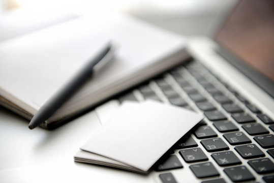 A business card and a paper notebook with a pen on a laptop keyboard. Shallow depth of field. - Powered by Adobe