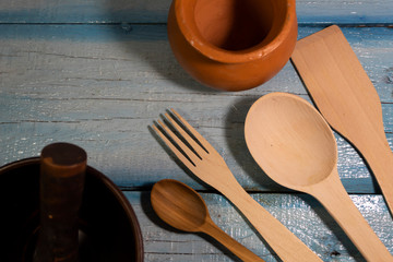 On a wooden background are wooden cutlery - a spatula,  two spoons, a fork. On the sides are two...