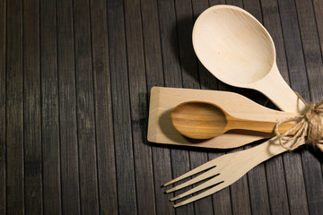 On a wooden dark background are wooden cutlery - small and large spoons, a fork, a spatula, tied with a hemp rope.