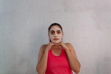 portrait of young hispanic woman wearing a hydrating and exfoliating face mask on a white background
