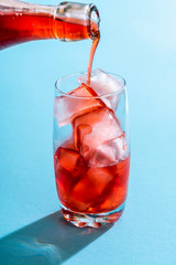 Pouring strawberry syrup over in a glass of water.