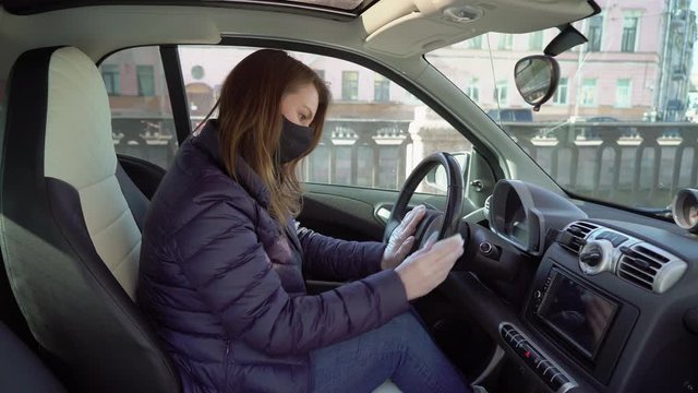 Young woman clean steering whell of car in protective gloves.