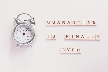 Alarm clock and words end of quarantine on pastel background. Creative flat lay, quarantine is over...