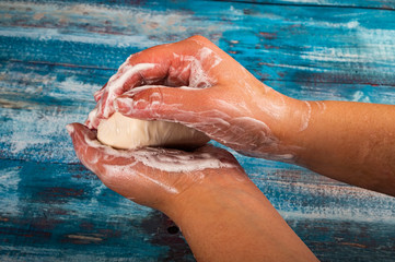 Fototapeta premium Someone is soaping their hands with a piece of toilet soap on a wooden background. Close up. Washing hands with soap is a prevention of COVID-19 infection.