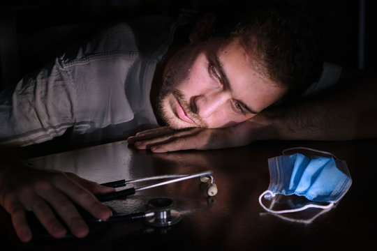 Coronavirus: Young bored and sad doctor with protective mask looking at the stethoscope