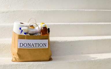 A donation bag / box, filled with food and cleaning supplies, sits outside on white steps after...