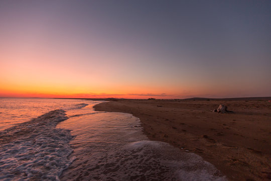 Incredibly beautiful sunset on the sea with pink and red sky, sun, and clean sand.