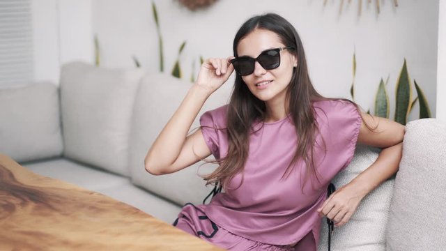 Portrait of beautiful woman in dark sunglasses sits in cafe, looking at camera