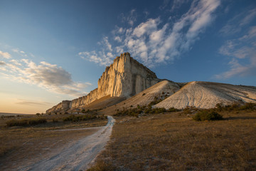 White rock against a beautiful sunset, light clouds fly over the rock and the road leads to the foot of the rock.