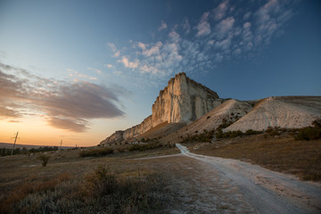 White rock against a beautiful sunset, light clouds fly over the rock and the road leads to the foot of the rock.