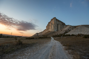 White rock against a beautiful sunset, light clouds fly over the rock and the road leads to the foot of the rock.