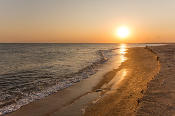 Incredibly beautiful sunset on the sea with pink and red sky, sun, and clean sand.