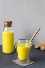 Golden milk is a delicious hot, traditional Indian drink for prevention and support of the immune system with turmeric root in a glass. A filled bottle and ginger are placed behind it. Copy space.