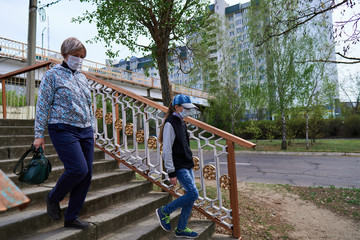 woman and child girl walks down the street during the day, a pedestrian walkway and buildings with apartments, a residential area, a medical mask on their faces protects against viruses and dust