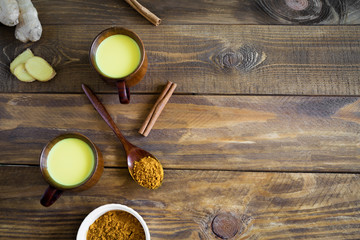 Hot Indian drink golden milk in two wooden cups on a background.Next to it are the ingredients...