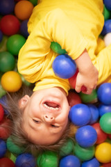 Fototapeta na wymiar Little girl in a ball pit smiling at the camera, having fun at the children play center