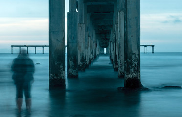 Two people stand on the beach on a cloudy day under the pier in San Diego