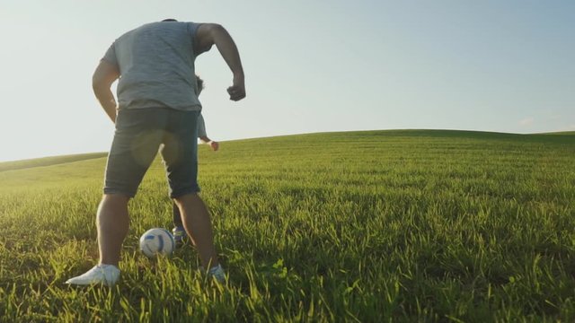 Father and his son playing together soccer football on field.
