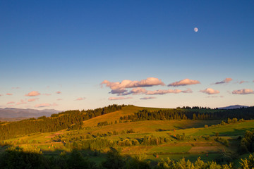 Fototapeta na wymiar Mountain landscape at sunset. The slopes of the mountains in the evening light. Moon in the evening sky over the mountains. Carpathian mountains