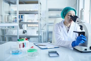 Naklejka premium Female doctor looking through the microscope and examining the analysis in the lab