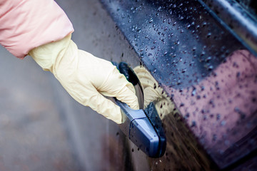 A woman's hand in a medical glove opens the car door . Opening the door in medical gloves . Clean hands. Protection from bacteria. Coronavirus and protection against it.