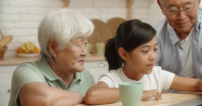 Senior asian couple together with their teen granddaughter who teaches them how to use a laptop, surfing through internet - family bonds and ties concept 4k footage