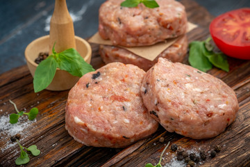 Homemade raw ground beef and Burger Patty with Basil, tomatoes and seasonings on a wooden Board.