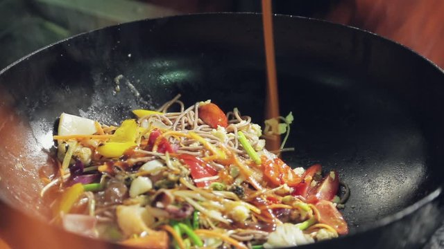 Chef cooks in fired up wok the noodles and Adds sauce and mixes it. Selective focus сlose-up.