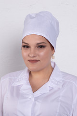 Portrait of attractive young female doctor in white medical jacket and  white medical cap on a grey background.