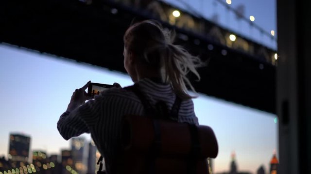 Concept of youth travelling and getaway journey, millennial female tourist using smartphone camera for photographing scenic cityscape during evening time and voyage trip near Manhattan island
