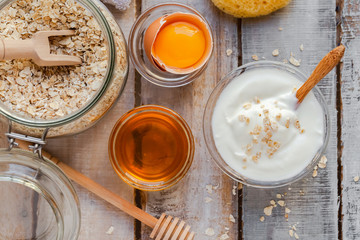 Concept of natural organic ingredients in cosmetology and gentle home treatment during quarantine. Do it yourselft. Handmade mask with honey, egg, oats. Wooden background. Flat lay top view close up