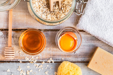 Concept of natural organic ingredients in cosmetology and gentle home treatment during quarantine. Do it yourselft. Handmade mask with honey, egg, oats. Wooden background. Flat lay top view close up