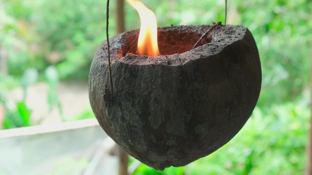 Homemade coconut candle hanging on a 
wire and swinging. Flame burns in half coconut shell, pendulum motion, slow motion. mistical ritual voodoo concept