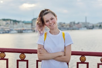 Outdoor portrait of smiling teenage girl of 15, 16 years old with folded arms