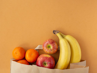 Eco paper bag with fruit banana, apple, tangerine on brown background. Concept of donation food, delivery service. Flat lay, top view, copy space