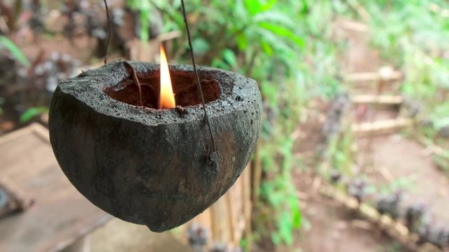 Homemade coconut candle hanging on a 
wire and swinging. Flame burns in half coconut shell, pendulum motion, slow motion. mistical ritual voodoo concept