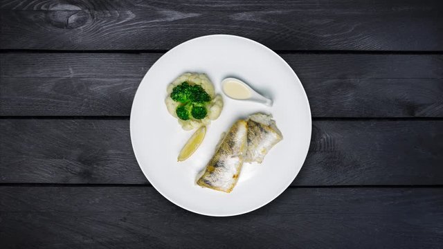 Pike perch fillet with broccoli and cauliflower Rotates on a plate. Black wooden background. Top view