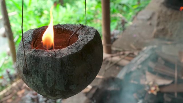 Homemade coconut candle hanging on a 
wire and swinging. Flame burns in half coconut shell, pendulum motion, slow motion. mistical ritual voodoo concept