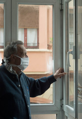Fototapeta na wymiar .lonely old man living the quarantine in his house this April. Old man longs for freedom at home while looking out the window at the street.elderly man with surgical mask at home