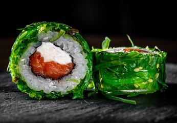 Sushi rolls with seafood, salmon, cream cheese and Chuka salad on black wooden table background